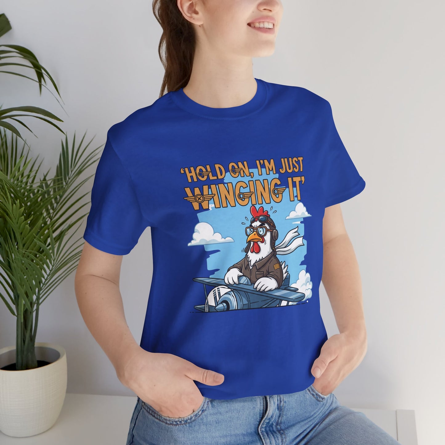Person wearing a blue t-shirt with a cartoon chicken graphic and text 'Hold on, I'm just winging it'.