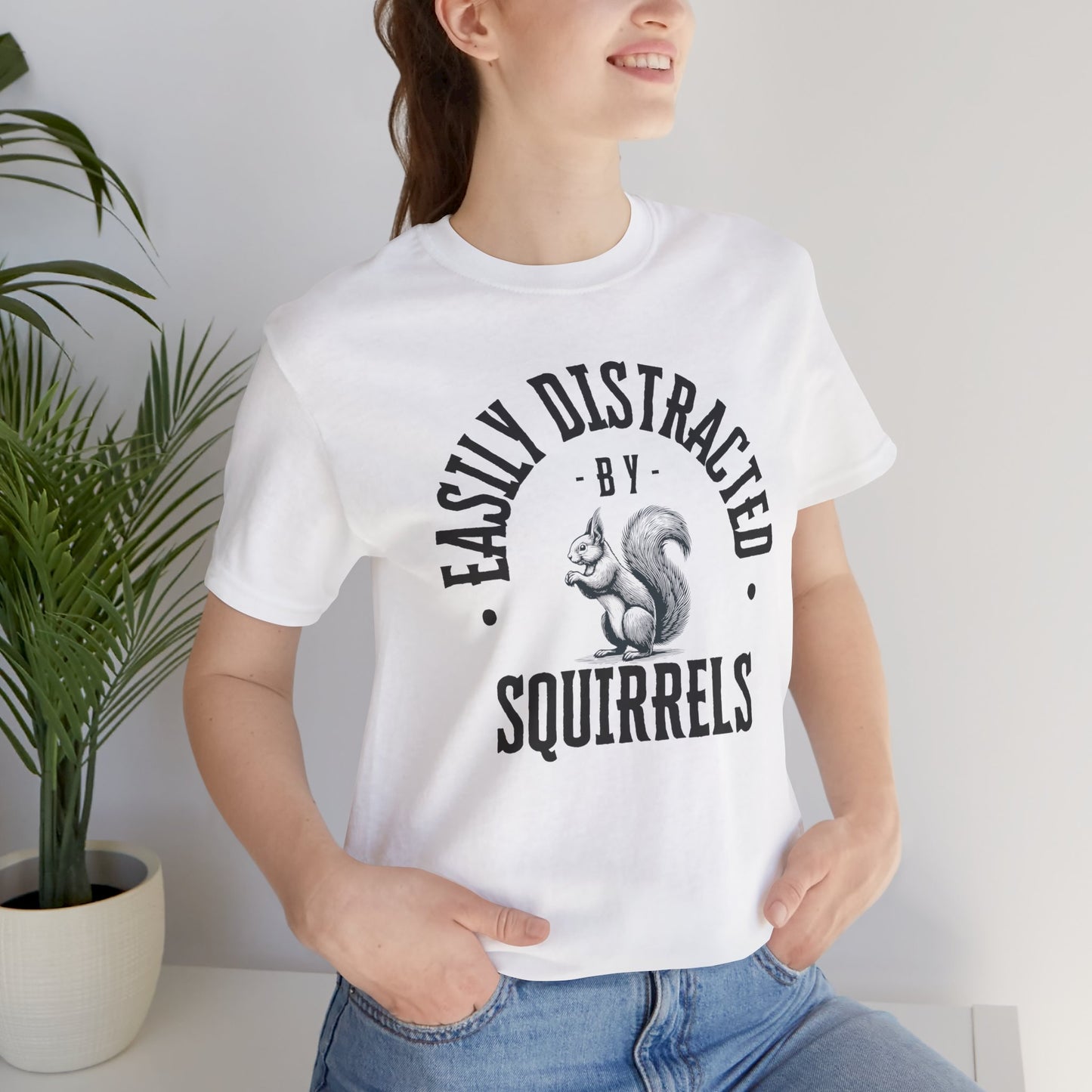 Person wearing a white t-shirt with a squirrel graphic and text 'EASILY DISTRACTED BY SQUIRRELS', standing against a plain background.