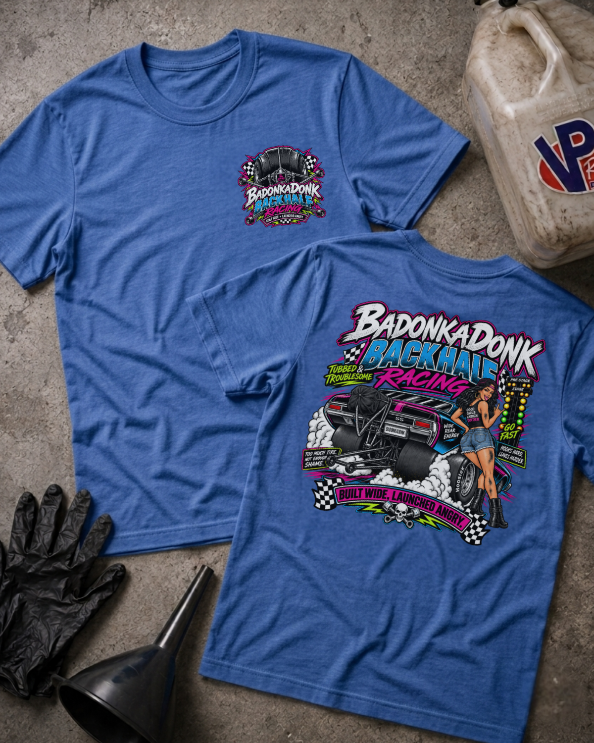 Two blue graphic T-shirts laid flat on a concrete surface, showing the front and back designs. The shirts feature a colorful 'Badonkadonk Backhalf Racing' graphic with a race car, checkered flags, and a woman.