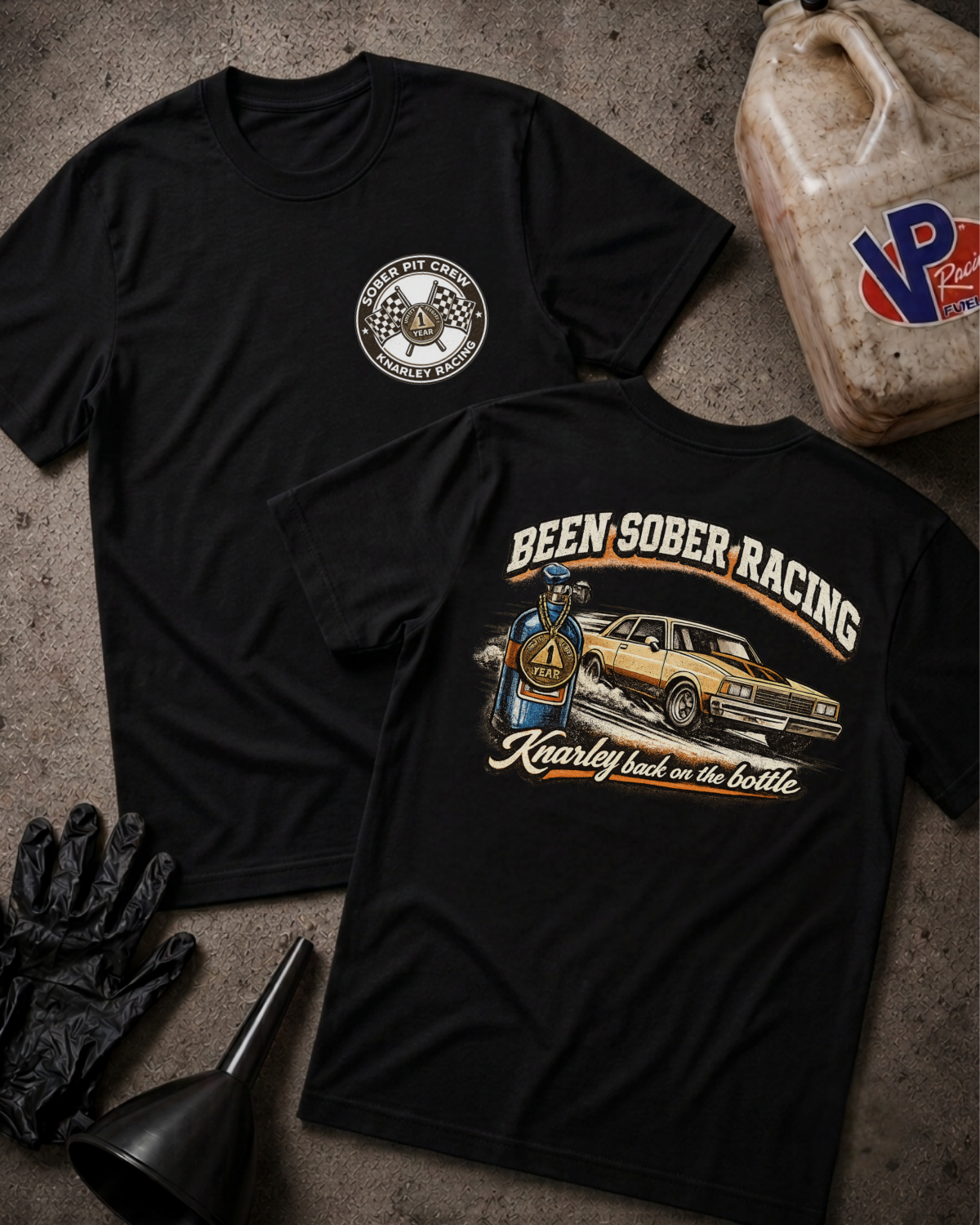 Two black graphic t-shirts displayed on a textured concrete surface with racing-themed props, including a gas can, gloves, funnel, and a race medallion. One shirt shows a circular chest logo, and the other shows a large back graphic reading 'Been Sober Racing' with a race car and driver illustration.