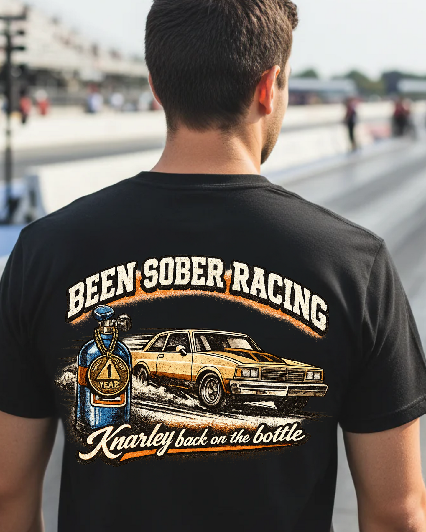 Person wearing a black t-shirt with 'Been Sober Racing' graphic at a race track.
