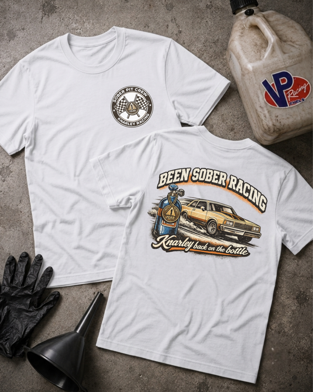 Two white graphic t-shirts displayed flat on a gray concrete surface, accompanied by racing-themed props including a VP Racing jug, black gloves, and a funnel. The front shirt features a circular logo, and the back shirt features a large graphic of a race car and the text 'Been Sober Racing'.