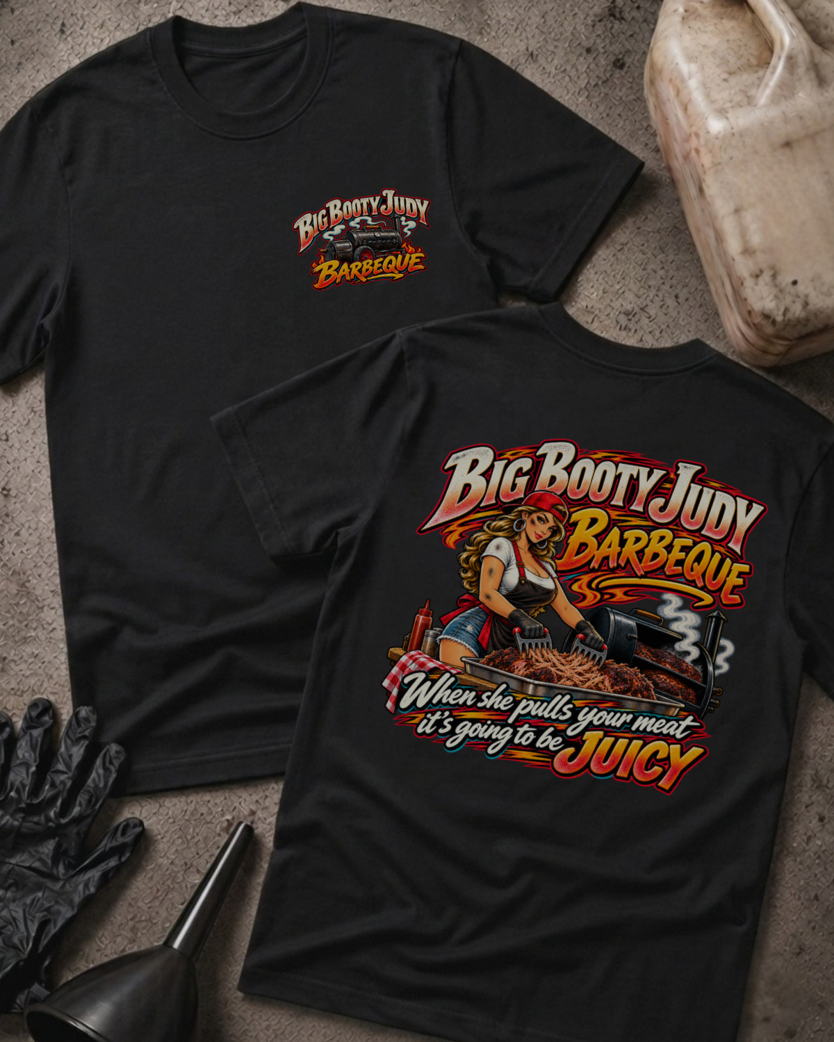 Big Booty Judy Barbeque Juicy T-shirt in black, flat lay showing the front chest logo and the back graphic reading Big Booty Judy Barbeque, When She Pulls Your Meat It's Going to Be Juicy, styled with work gloves, a funnel, and a fluid jug.
