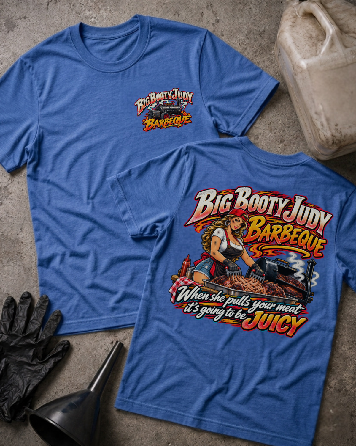 Big Booty Judy Barbeque Juicy T-shirt in heather true royal, flat lay showing the front chest logo and the back graphic reading Big Booty Judy Barbeque, When She Pulls Your Meat It's Going to Be Juicy, styled with work gloves, a funnel, and a fluid jug.
