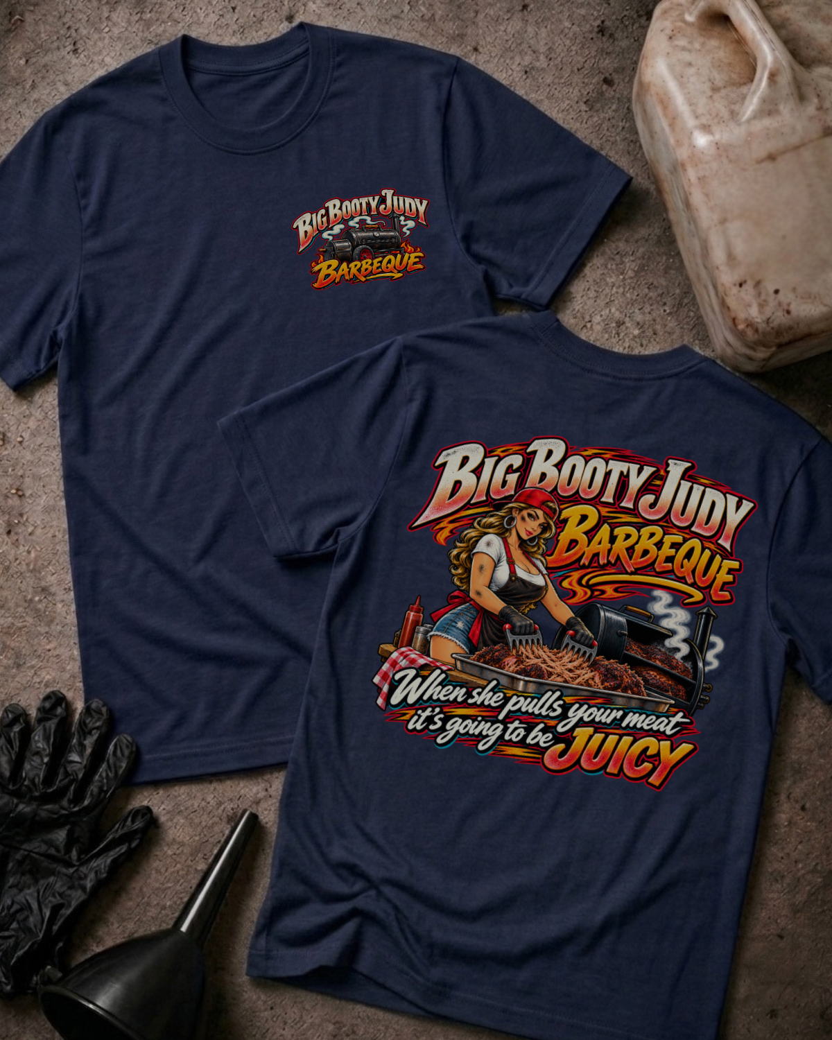 Big Booty Judy Barbeque Juicy T-shirt in navy, flat lay showing the front chest logo and the back graphic reading Big Booty Judy Barbeque, When She Pulls Your Meat It's Going to Be Juicy, styled with work gloves, a funnel, and a fluid jug.