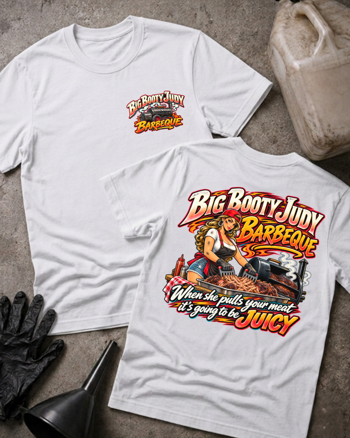 Big Booty Judy Barbeque Juicy T-shirt in white, flat lay showing the front chest logo and the back graphic reading Big Booty Judy Barbeque, When She Pulls Your Meat It's Going to Be Juicy, styled with work gloves, a funnel, and a fluid jug.