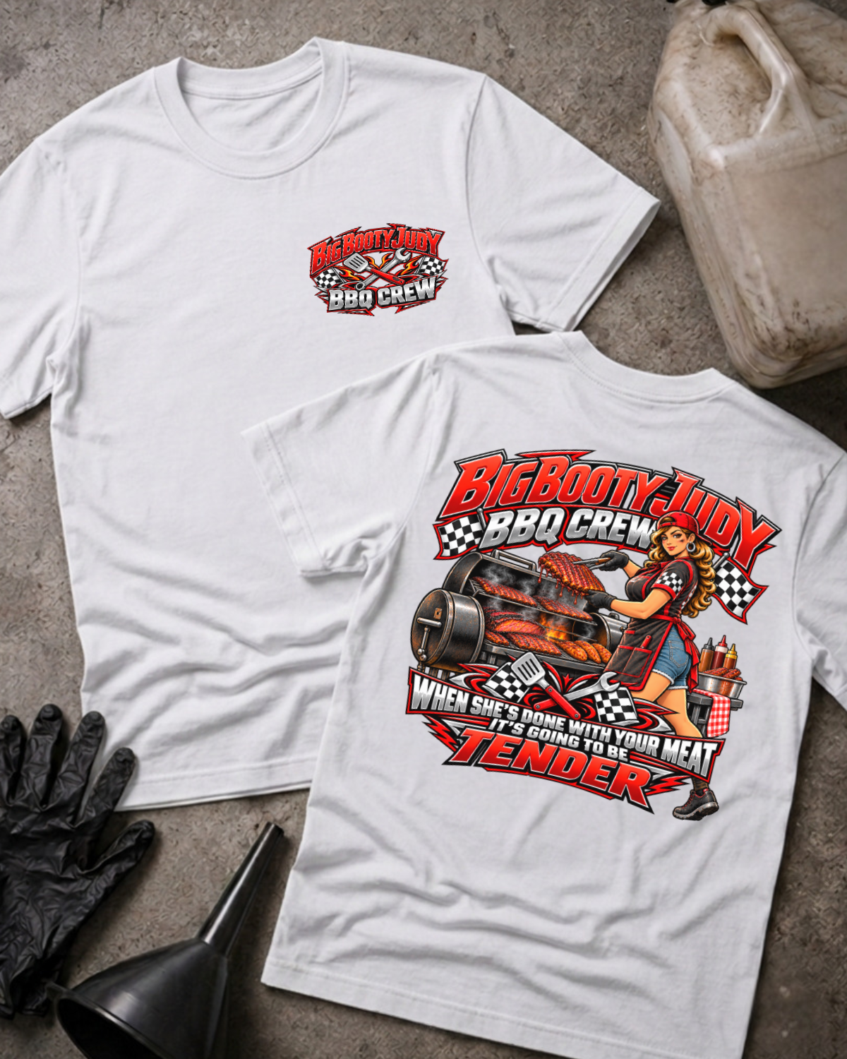 Big Booty Judy BBQ Crew T-shirt in white, flat lay showing the front chest logo and the back graphic reading Big Booty Judy BBQ Crew, When She's Done With Your Meat It's Going to Be Tender, styled with work gloves, a funnel, and a fluid jug.