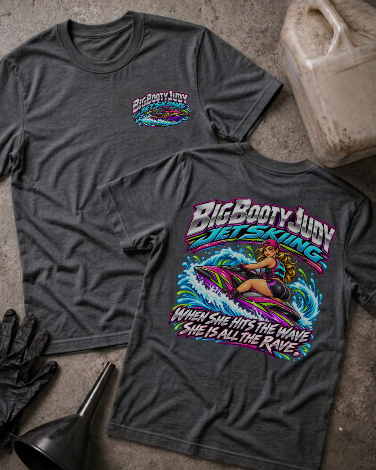 Dark grey heather Big Booty Judy Jet Skiing T-shirt, showing a small front chest logo and colorful back graphic of Judy riding a jet ski with “When she hits the wave she is all the rave.”