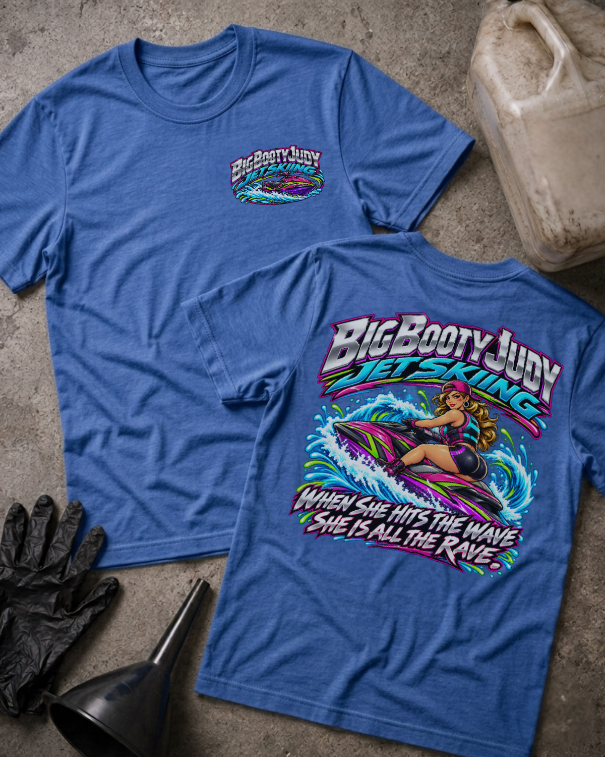 Heather true royal blue Big Booty Judy Jet Skiing T-shirt, showing a small front chest logo and colorful back graphic of Judy riding a jet ski with “When she hits the wave she is all the rave.”