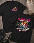 Two black graphic T-shirts laid flat on a textured gray surface, with racing-themed artwork and text. One shirt shows a small chest graphic, and the other shows a large back graphic with the words 'Big Booty Judy Racing Club' and 'Thick Slicks, Fast Time, and Bad Decisions'.