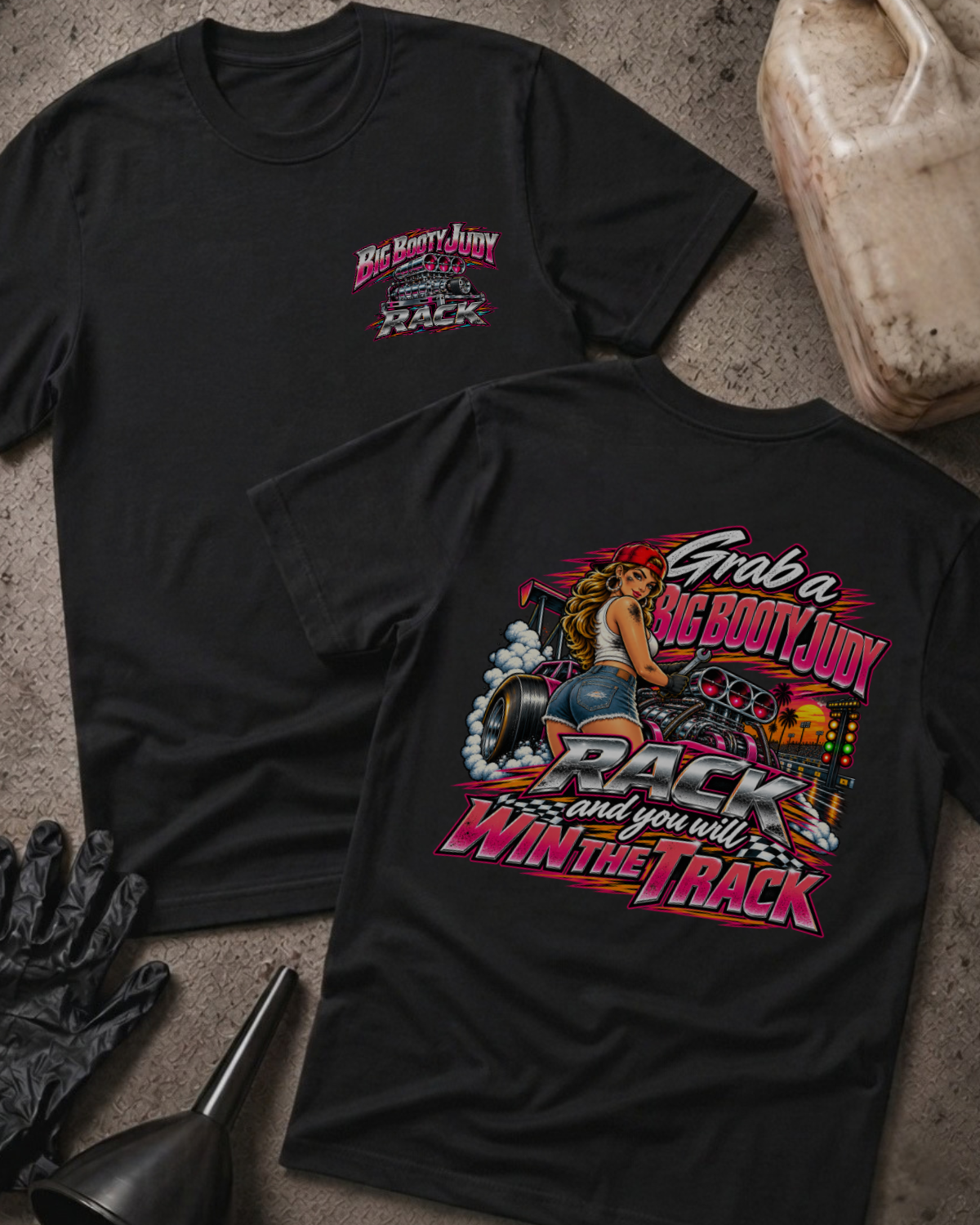 Big Booty Judy Rack To Win The Track T-shirt in black, flat lay showing the front chest logo and the back graphic reading Grab a Big Booty Judy Rack and You Will Win the Track, styled with work gloves, a funnel, and a fluid jug.
