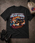 A black graphic t-shirt laid flat on a textured gray surface, surrounded by racing-themed props including a black oil funnel, a black glove, and a plastic jug of VP Racing. The t-shirt features a large graphic of a pin-up girl and a race car with the text 'BIG BOOTYJUDY REAR ENDS' and 'You'll be slamming it out the back of the Track'.