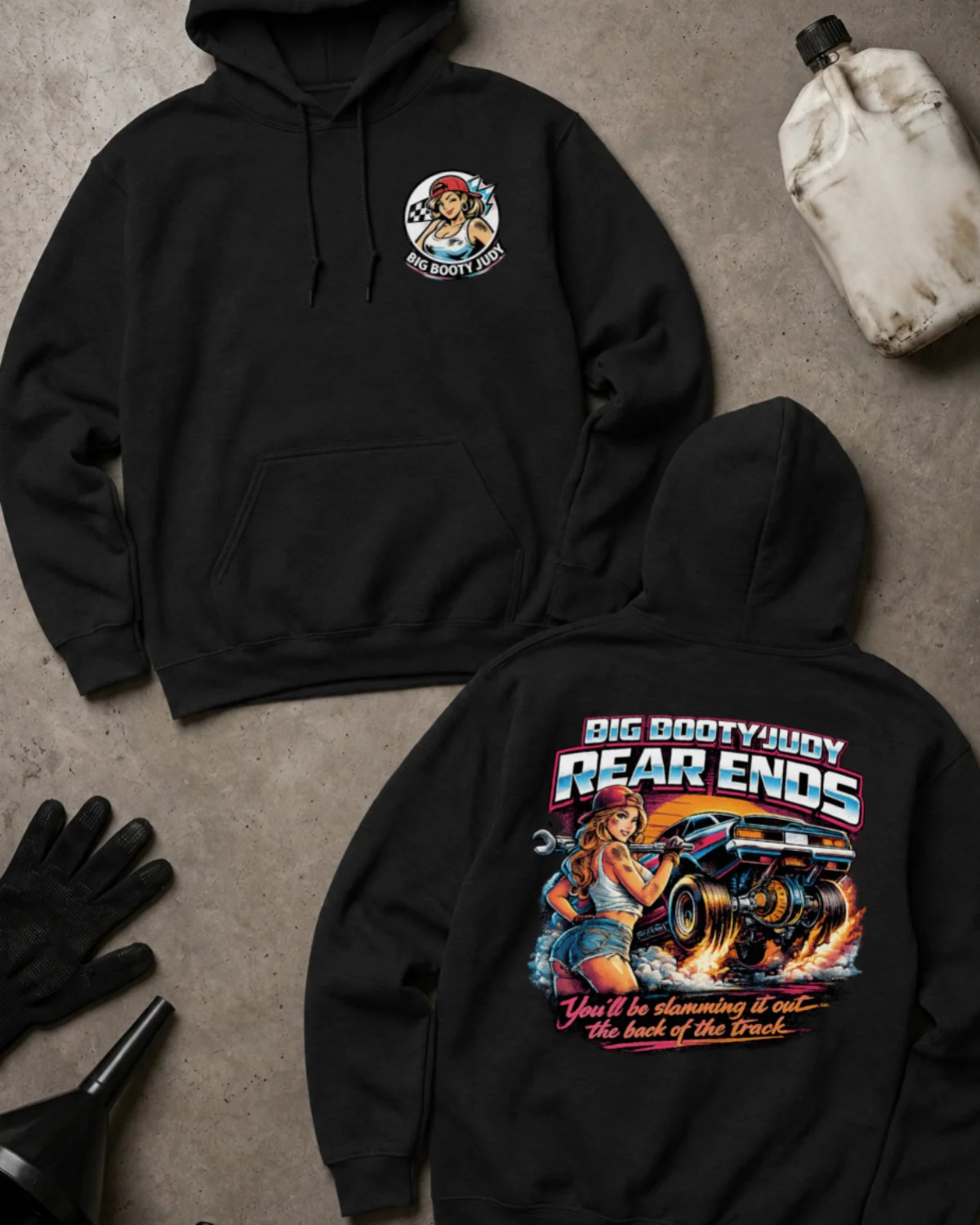 Two black hoodies laid flat on a gray concrete-style surface, showing the front and back of the same design. The front has a small circular chest graphic, and the back has a large colorful graphic with the text 'BIG BOOTYJUDY REAR ENDS' and additional stylized text below.
