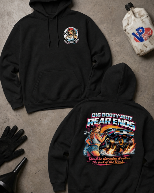 Two black hoodies laid flat on a gray concrete-style surface, showing the front and back of the same design. The front has a small circular chest graphic, and the back has a large colorful graphic with the text 'BIG BOOTYJUDY REAR ENDS' and additional stylized text below.