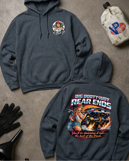 Two dark heather gray hoodies displayed on a concrete floor, one showing the front chest graphic and the other the back with a large truck graphic and text. A white jug, black gloves, and a funnel are arranged around them as styled props.