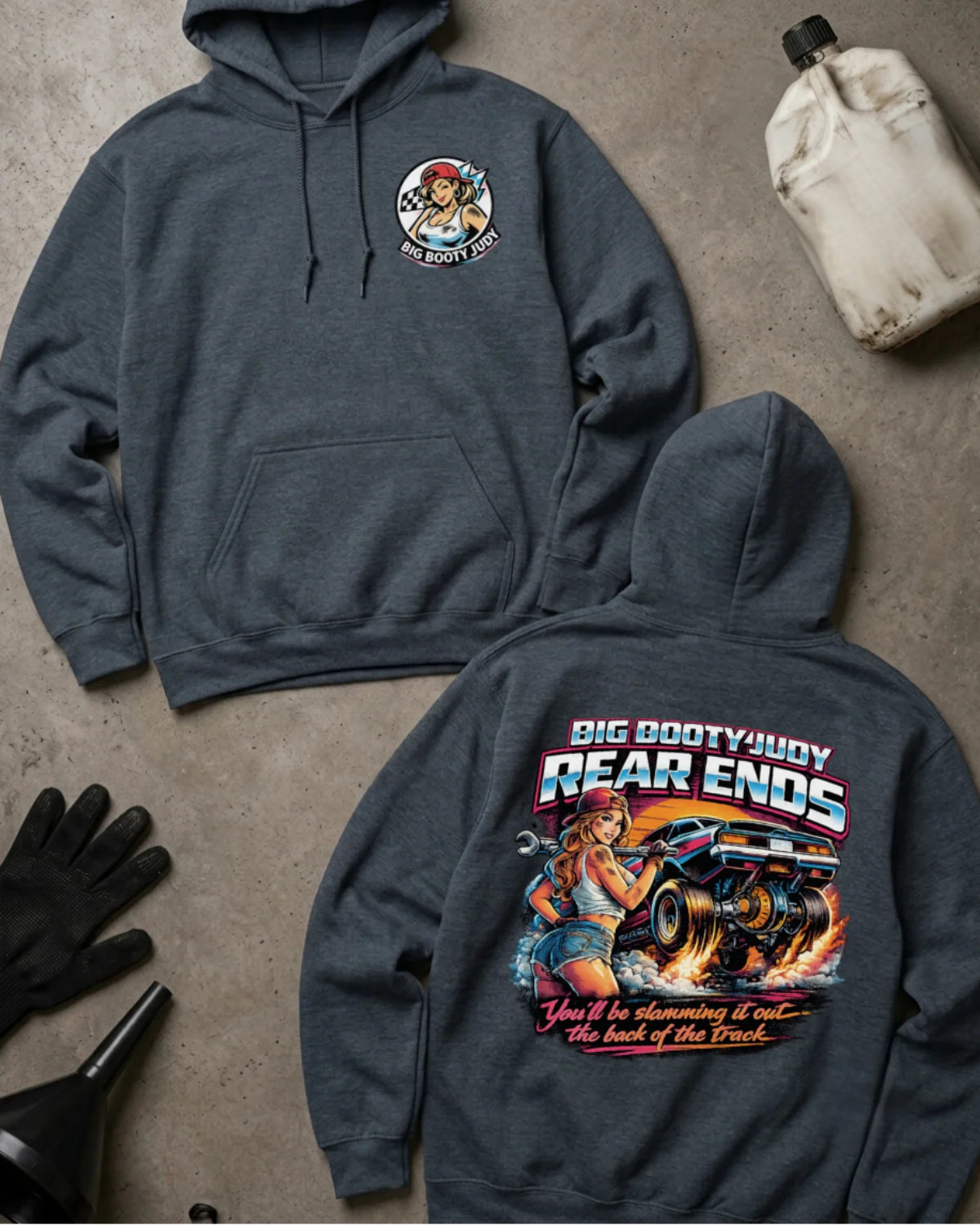 Two dark heather hoodies laid flat on a gray concrete-style surface, showing the front and back of the same design. The front has a small circular chest graphic, and the back has a large colorful graphic with the text 'BIG BOOTYJUDY REAR ENDS' and additional stylized text below.