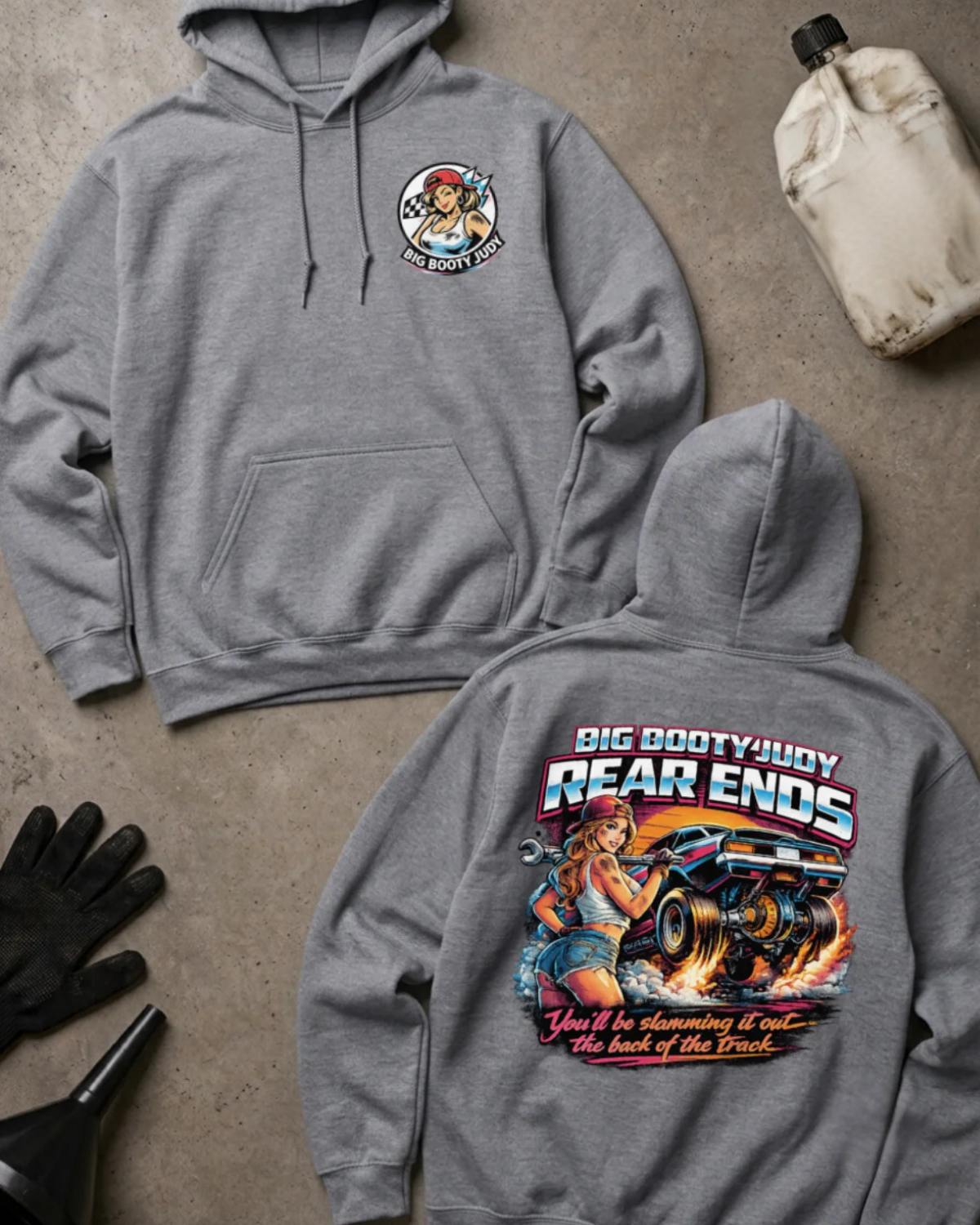 Two sport grey hoodies laid flat on a gray concrete-style surface, showing the front and back of the same design. The front has a small circular chest graphic, and the back has a large colorful graphic with the text 'BIG BOOTYJUDY REAR ENDS' and additional stylized text below.