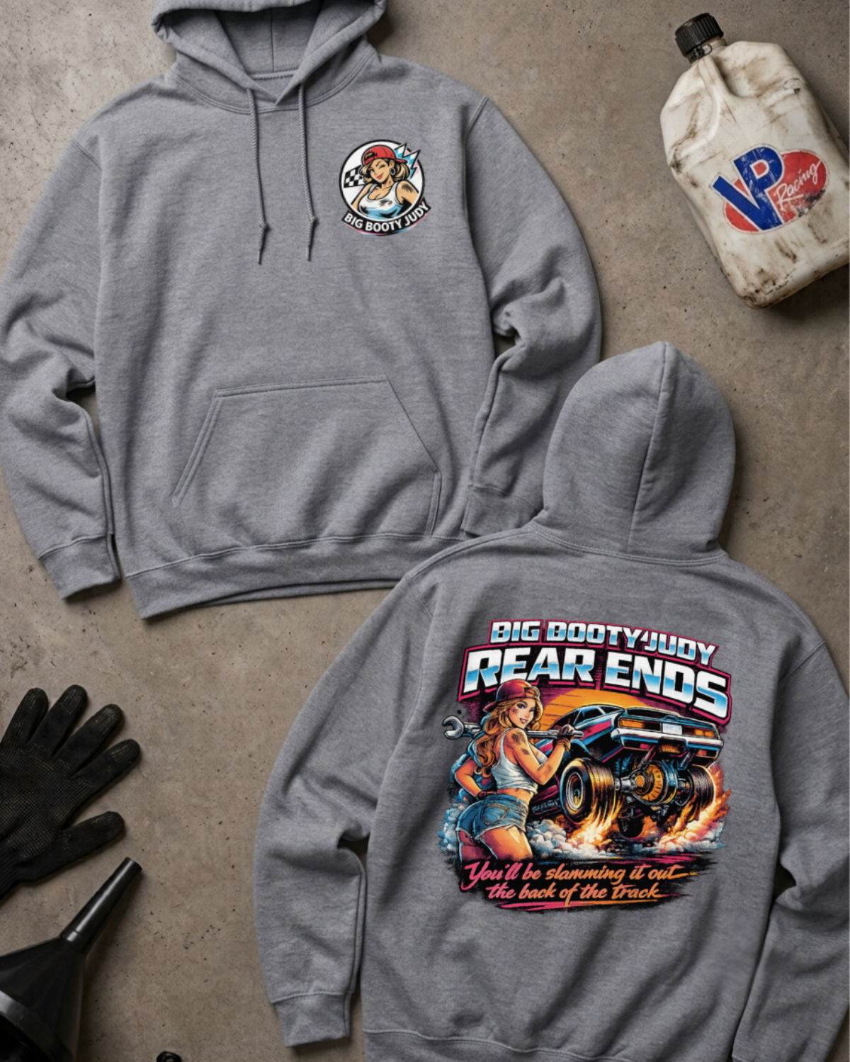Two heather gray hoodies laid flat on a concrete-style surface, one showing the front chest graphic and the other the large back graphic. The graphics feature a cartoon truck and the text 'Big Booty Judy Rear Ends' with additional decorative text below.