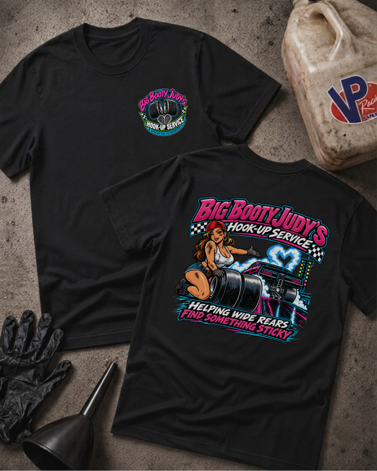 Two black graphic t-shirts showing a 'BIG BOOTY JUDY HOOK-UP SERVICE' logo on the front and a colorful graphic of a woman with racing slicks and 'BIG BOOTY JUDY'S HOOK-UP SERVICE HELPING WIDE REARS FIND SOMETHING STICKY' text on the back