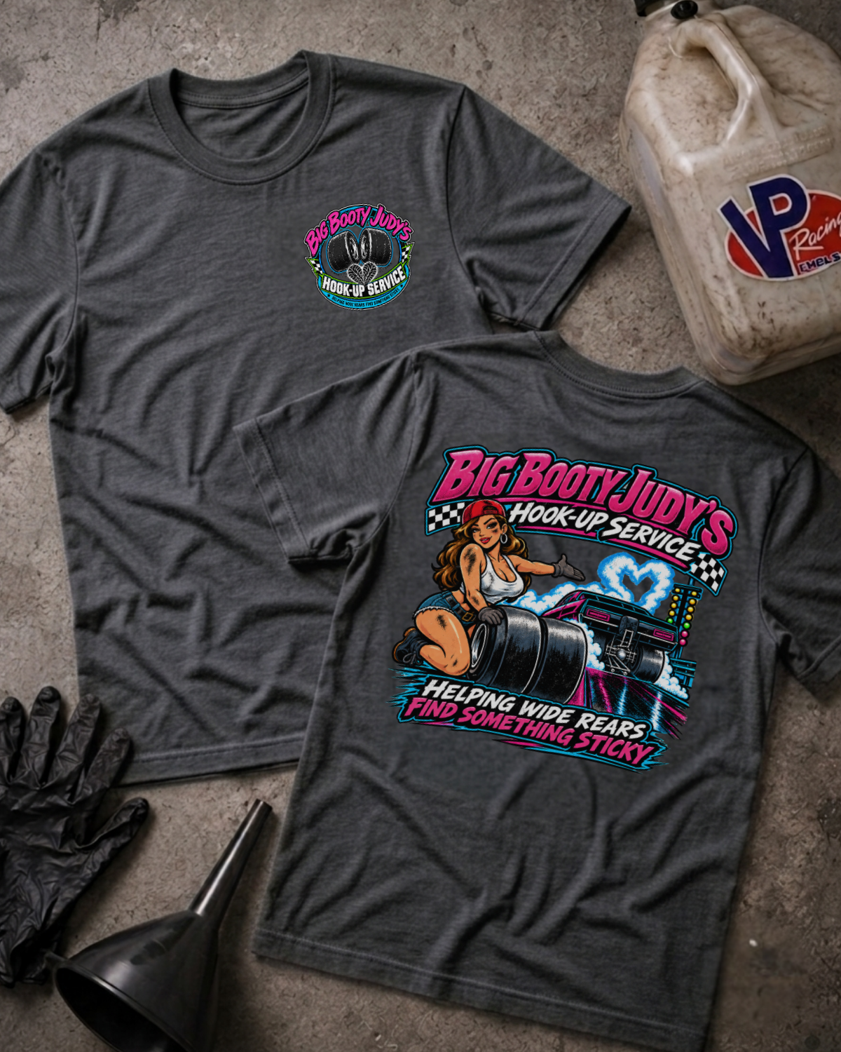 Two dark grey heather graphic t-shirts showing a 'BIG BOOTY JUDY HOOK-UP SERVICE' logo on the front and a colorful graphic of a woman with racing slicks and 'BIG BOOTY JUDY'S HOOK-UP SERVICE HELPING WIDE REARS FIND SOMETHING STICKY' text on the back