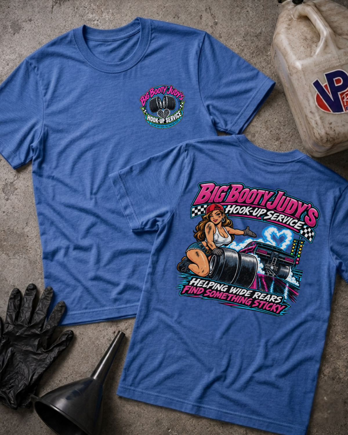 Two heather true royal graphic t-shirts showing a 'BIG BOOTY JUDY HOOK-UP SERVICE' logo on the front and a colorful graphic of a woman with racing slicks and 'BIG BOOTY JUDY'S HOOK-UP SERVICE HELPING WIDE REARS FIND SOMETHING STICKY' text on the back