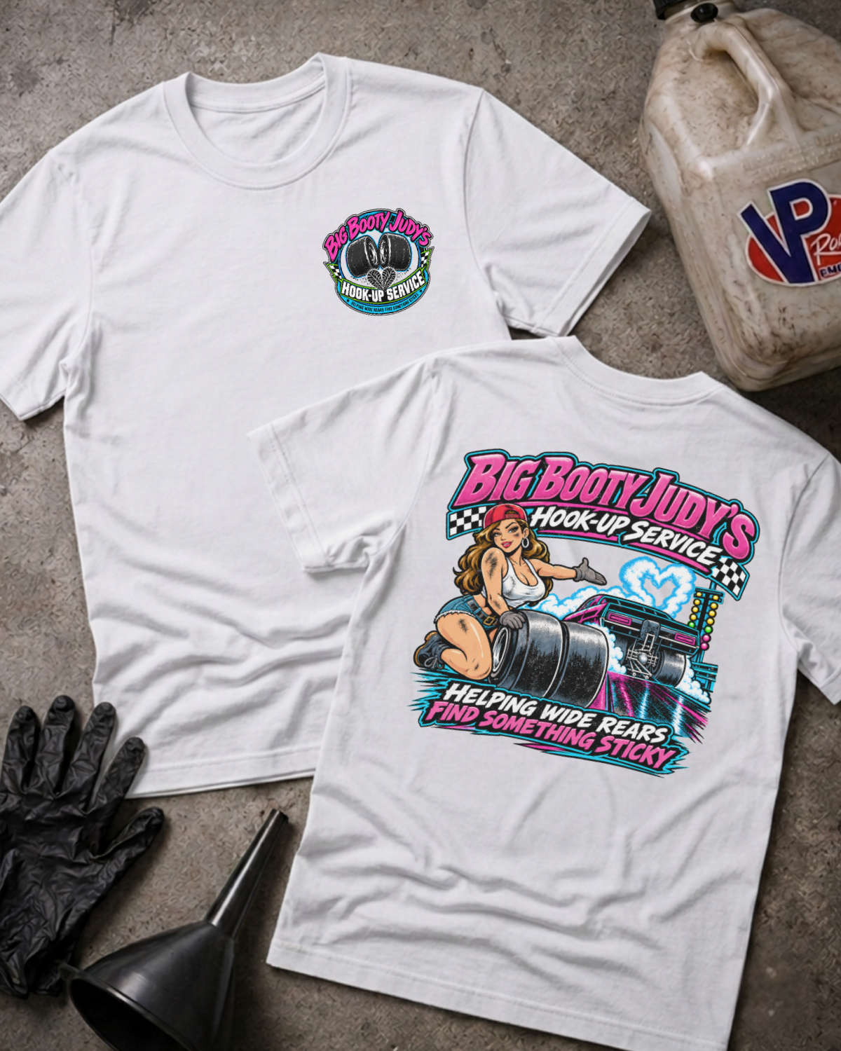 Two white graphic t-shirts showing a 'BIG BOOTY JUDY HOOK-UP SERVICE' logo on the front and a colorful graphic of a woman with racing slicks and 'BIG BOOTY JUDY'S HOOK-UP SERVICE HELPING WIDE REARS FIND SOMETHING STICKY' text on the back