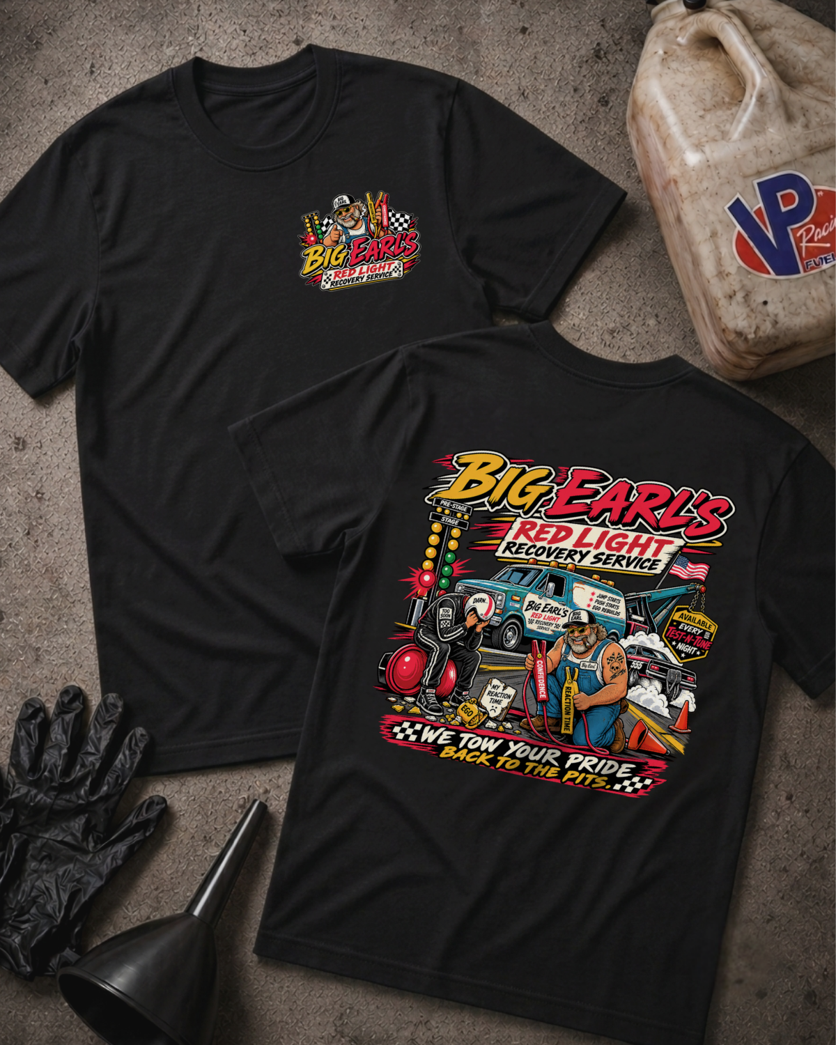A black short-sleeve t-shirt with a large, colorful graphic print on the front. The graphic features a cartoon illustration of a race car, tow truck, and recovery workers under the text 'Big Earl's Red Light Recovery Service' and 'We Tow Your Pride Back to the Pit'.