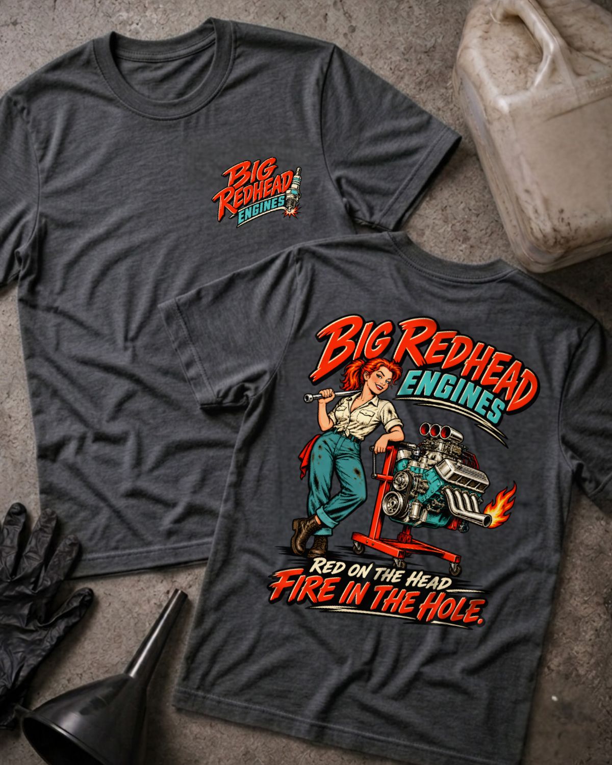 Dark grey heather Big Redhead Engines T-shirt showing the front spark-plug logo and back cartoon of a redhead woman by an engine stand with a supercharged V8 and flaming headers, “Red on the Head, Fire in the Hole,” with gloves, funnel, and oil jug.