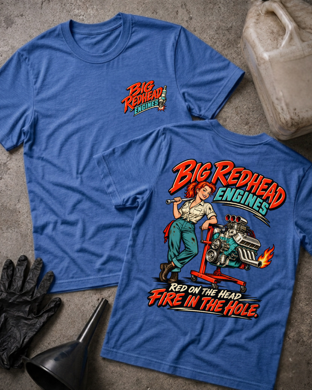 Heather royal blue Big Redhead Engines T-shirt showing the front spark-plug logo and back cartoon of a redhead woman by an engine stand with a supercharged V8 and flaming headers, “Red on the Head, Fire in the Hole,” with gloves, funnel, and oil jug.