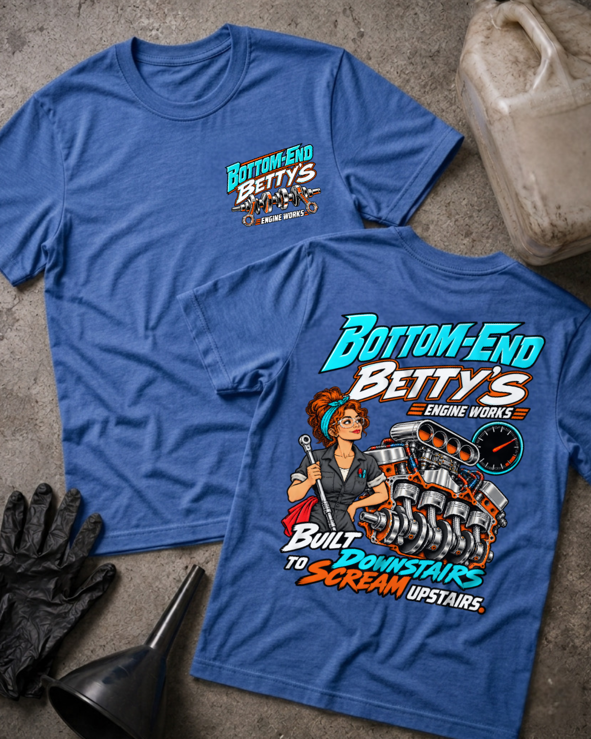 Heather royal blue Bottom End Betty’s Engine Works T-shirt showing the front chest logo and back cartoon of a woman mechanic with a torque wrench by a V8 engine’s crankshaft and pistons, “Built Downstairs to Scream Upstairs,” with gloves, funnel, and oil jug.