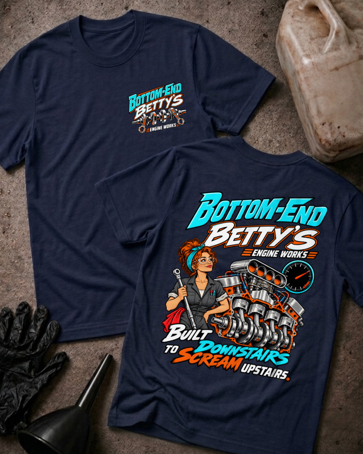 Navy Bottom End Betty’s Engine Works T-shirt showing the front chest logo and back cartoon of a woman mechanic with a torque wrench by a V8 engine’s crankshaft and pistons, “Built Downstairs to Scream Upstairs,” with gloves, funnel, and oil jug.