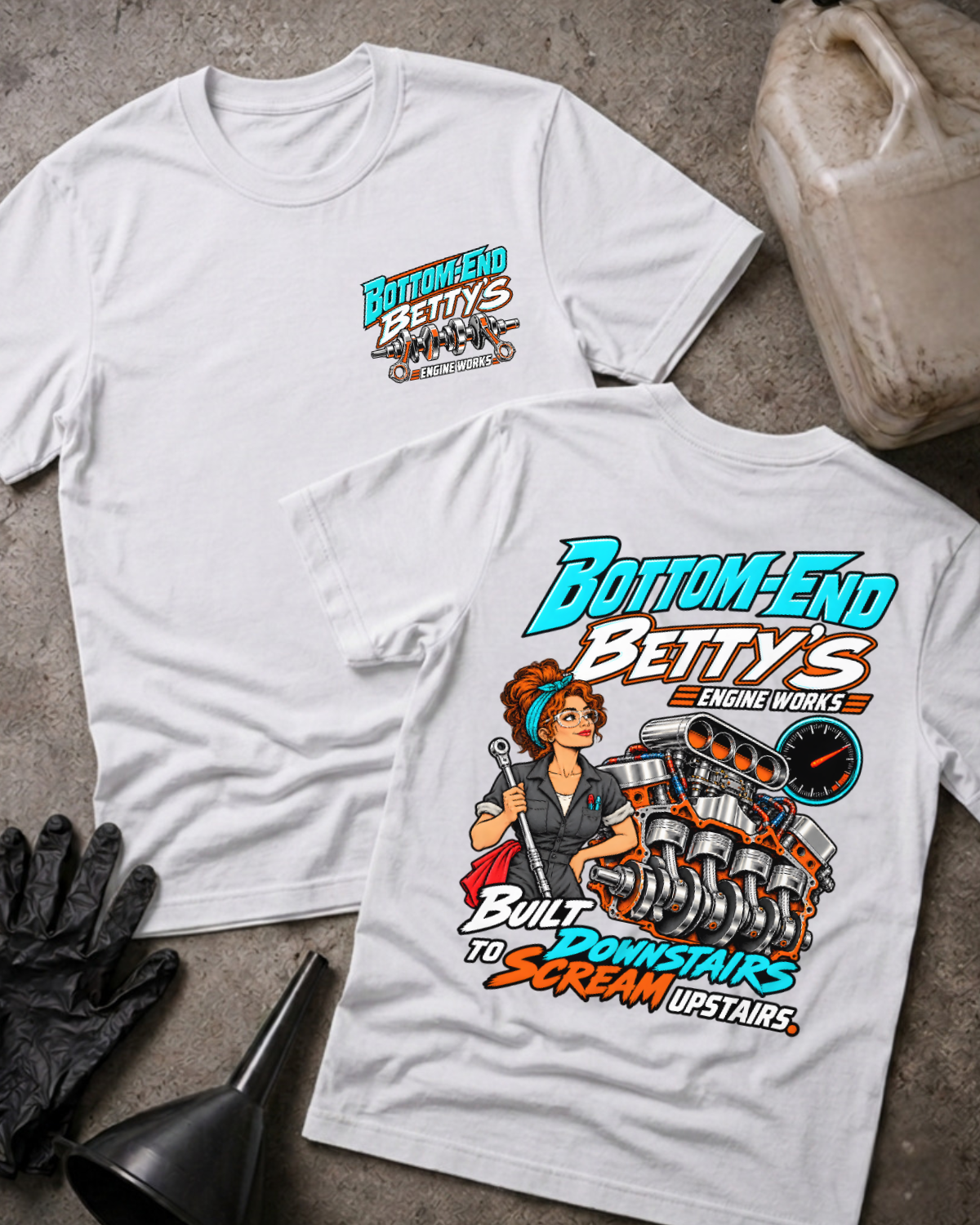 White Bottom End Betty’s Engine Works T-shirt showing the front chest logo and back cartoon of a woman mechanic with a torque wrench by a V8 engine’s crankshaft and pistons, “Built Downstairs To Scream Upstairs,” with gloves, funnel, and oil jug.
