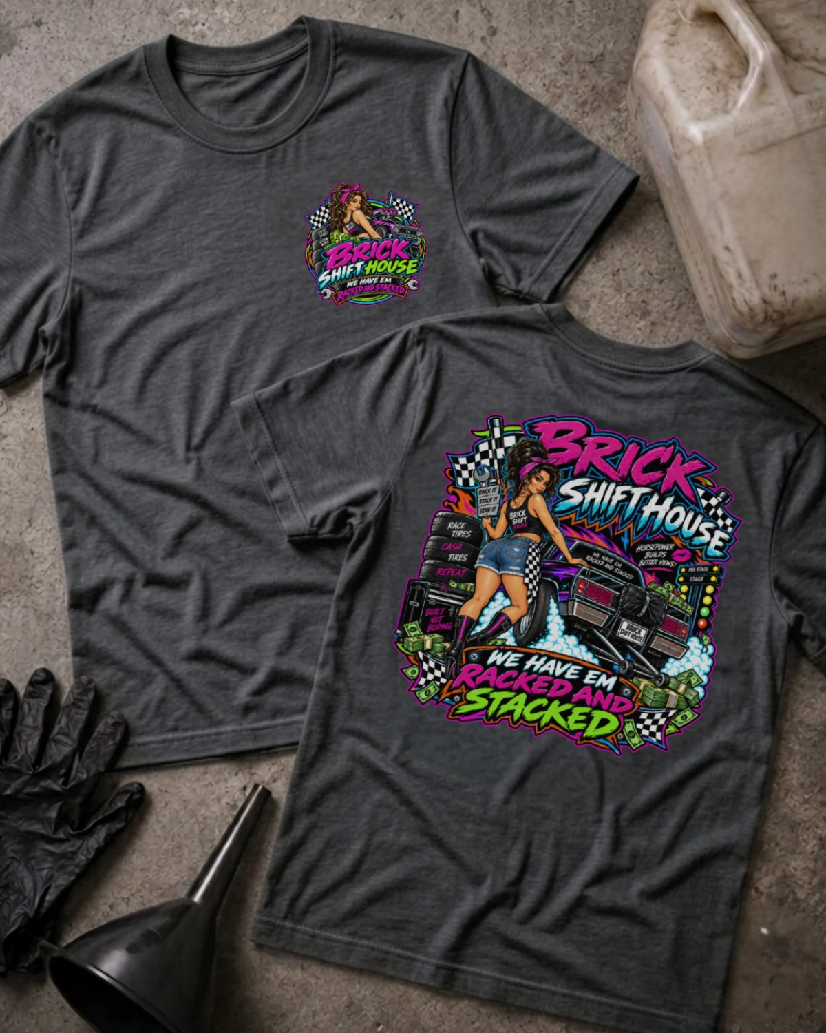 Front and back of Brick Shift House dark grey heather T-shirt with chest logo, woman beside stacked racing tires and a drag car, and “We have ’em racked and stacked” slogan.