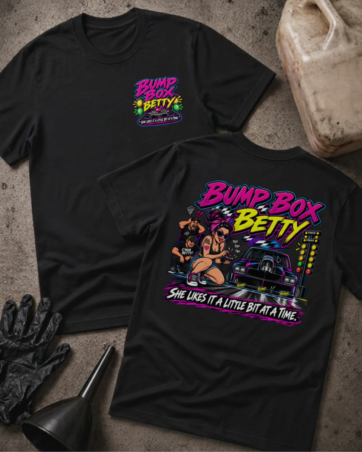 Front and back of Bump Box Betty black T-shirt with chest logo, woman using a handheld controller beside a drag car and staging lights, and “She likes it a little bit at a time” slogan.