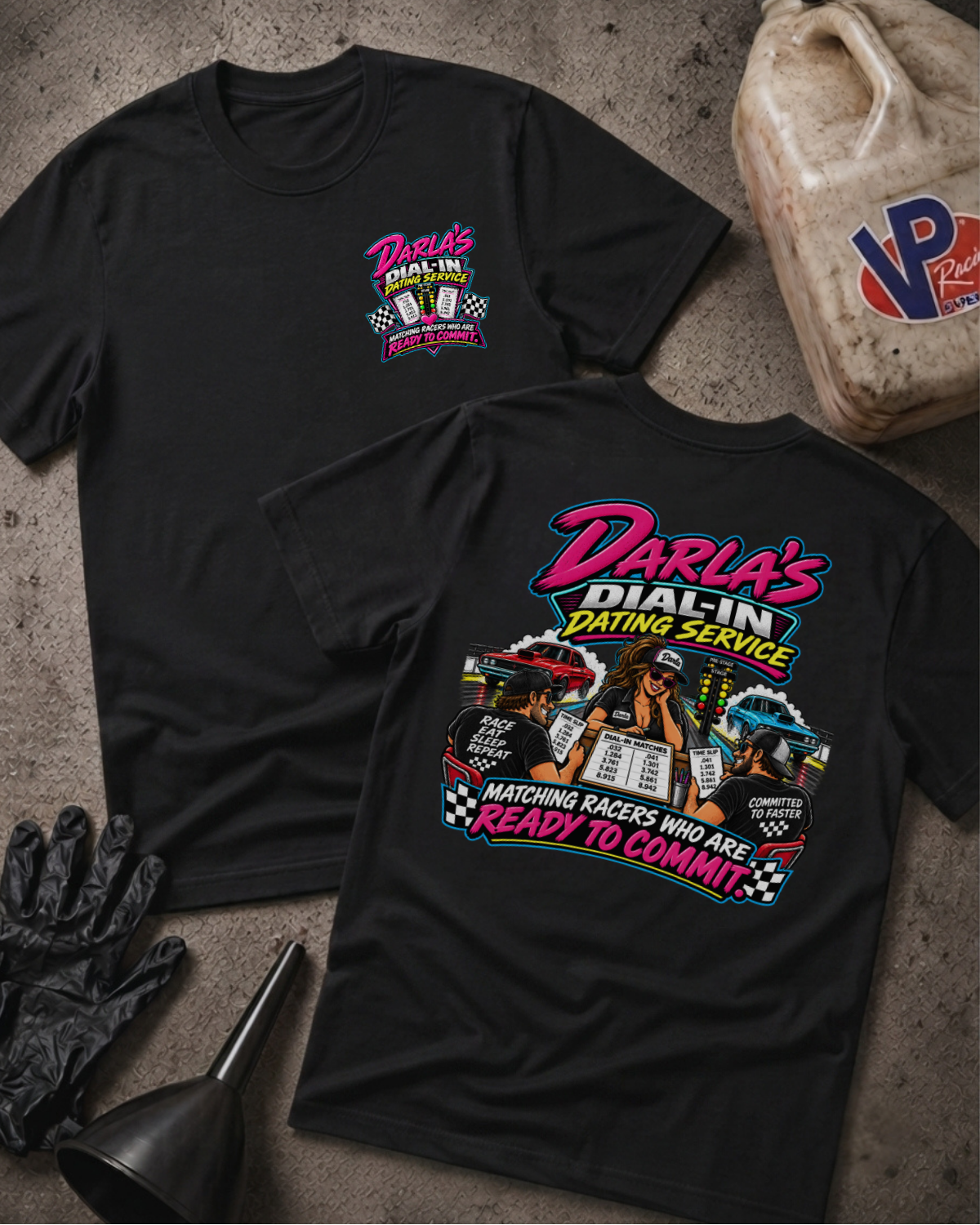 Two black graphic T-shirts laid flat on a concrete surface, with a vintage oil jug, black gloves, and funnel as styled props. The front shirt shows a small pink and yellow chest graphic reading Darla's Dial-In Dating Service, and the back shirt shows a large multicolor racing-themed graphic with the same brand text.