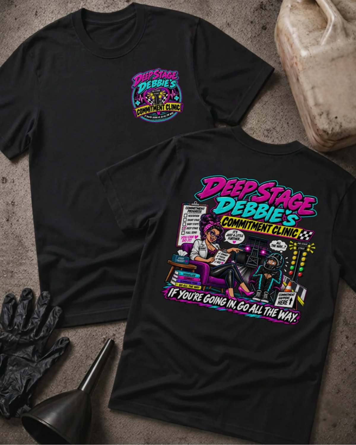 Front and back of Deep Stage Debbie’s Commitment Clinic black T-shirt with chest logo, woman counseling a helmeted racer beside staging lights, and “If you’re going in, go all the way” slogan.