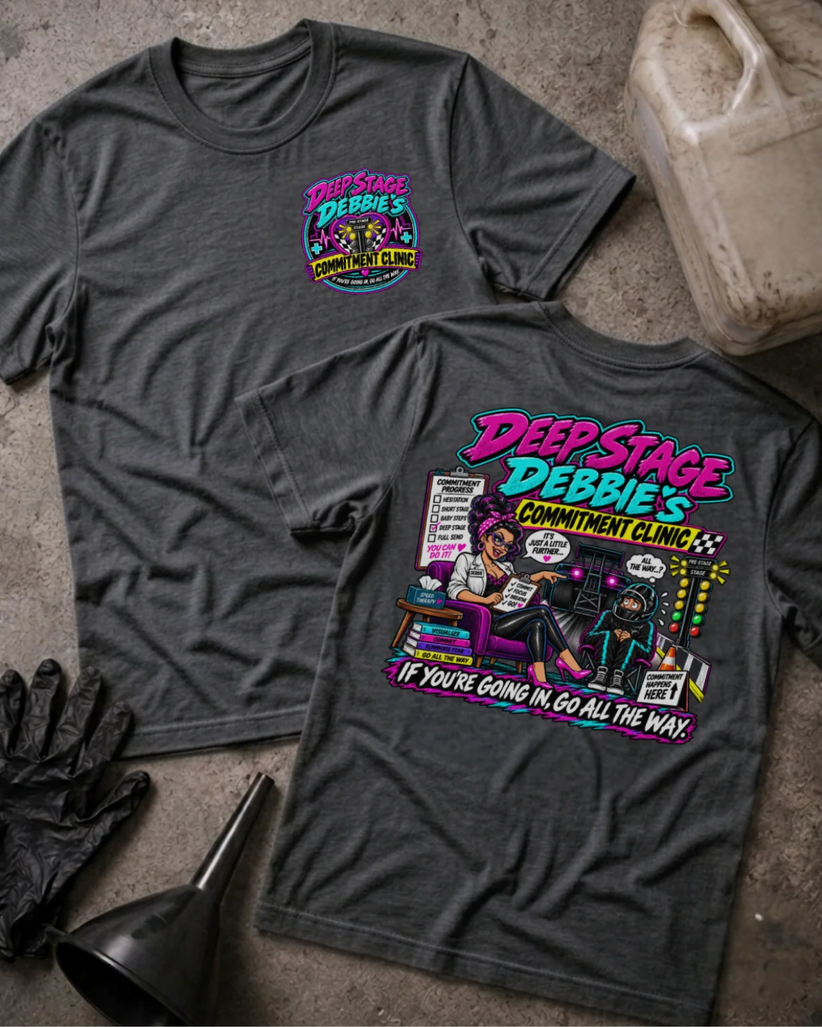 Front and back of Deep Stage Debbie’s Commitment Clinic dark grey heather T-shirt with chest logo, woman counseling a helmeted racer beside staging lights, and “If you’re going in, go all the way” slogan.
