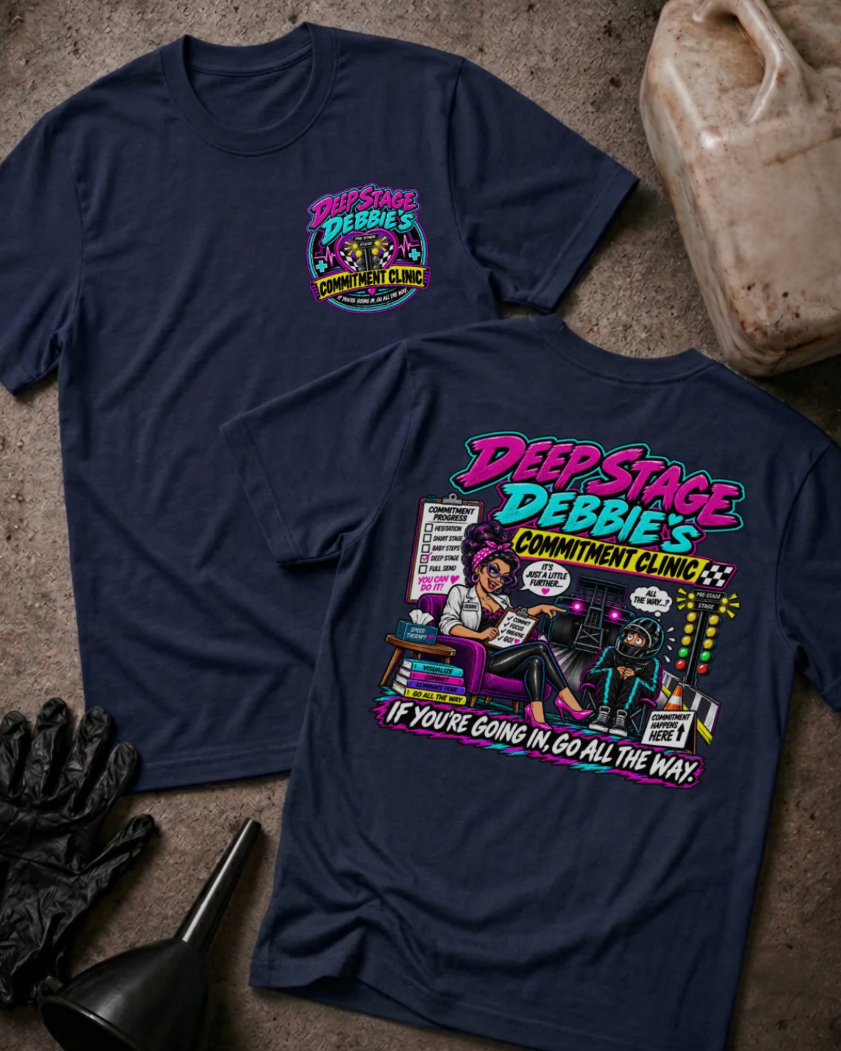 Front and back of Deep Stage Debbie’s Commitment Clinic navy T-shirt with chest logo, woman counseling a helmeted racer beside staging lights, and “If you’re going in, go all the way” slogan.