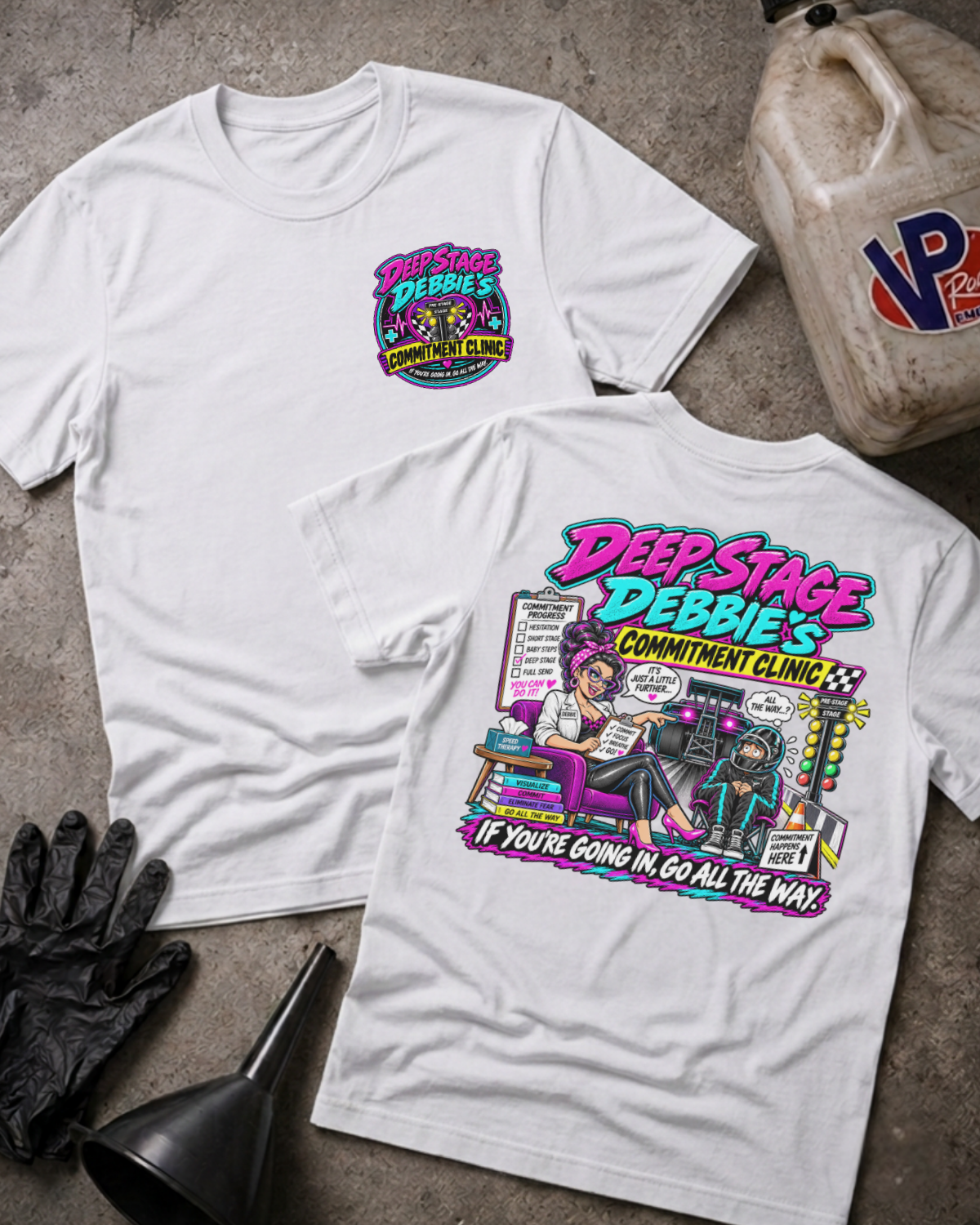Two white graphic T-shirts displayed on a concrete floor, with a black funnel, black gloves, and a plastic fuel container as props. The front shirt shows a small colorful chest graphic, and the back shirt shows a large colorful graphic with the text 'Deep Stage Debbie's Commitment Clinic' and 'If you're going in, go all the way.