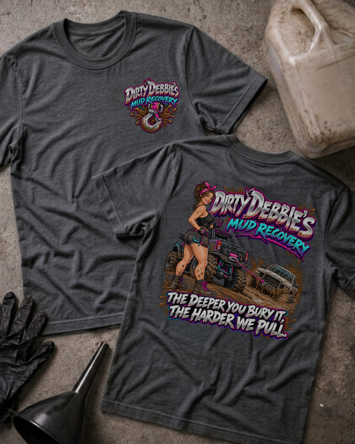 Dark grey heather Dirty Debbie’s Mud Recovery T-shirt, front and back views with a chest tow-hook logo and a woman beside trucks in mud, plus “The deeper you bury it, the harder we pull.”
