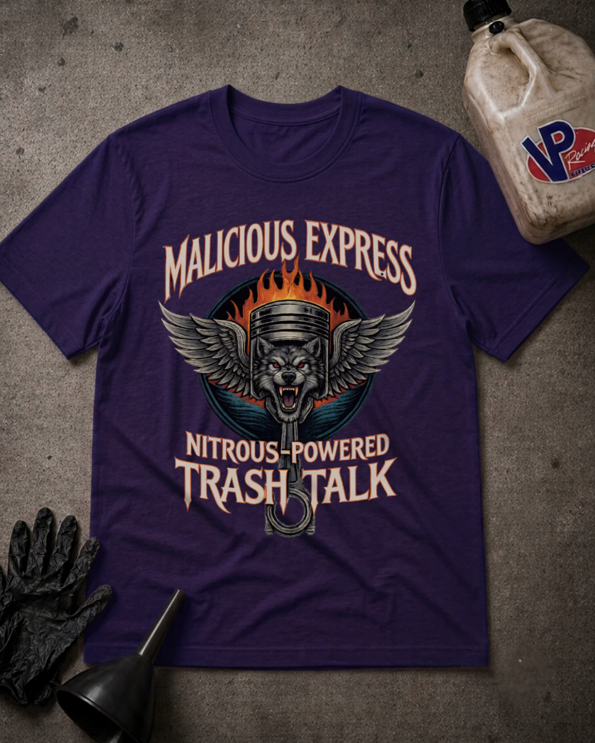 A purple graphic t-shirt laid flat on a textured gray surface, surrounded by motorcycle-themed props including a black glove, funnel, and a plastic jug. The shirt features a graphic of a skull wearing a piston helmet with wings, and the text 'MALICIOUS EXPRESS' and 'NITROUS-POWERED TRASH TALK'.