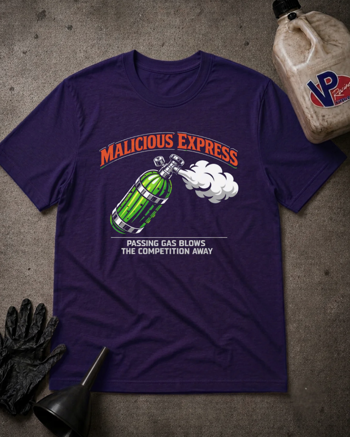 A purple short-sleeve graphic T-shirt laid flat on a gray textured surface, surrounded by black gloves, a black funnel, and a beige plastic jug with a visible VP logo. The shirt graphic reads "MALICIOUS EXPRESS" in orange above a green gas cylinder with white smoke, and smaller white text below.