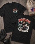 Two black graphic T-shirts laid flat on a textured gray surface, with racing-themed printed artwork and 'Drag Wife Putting You In The Groove' text. A black glove, funnel, and a plastic fuel can are placed around them as styled props.