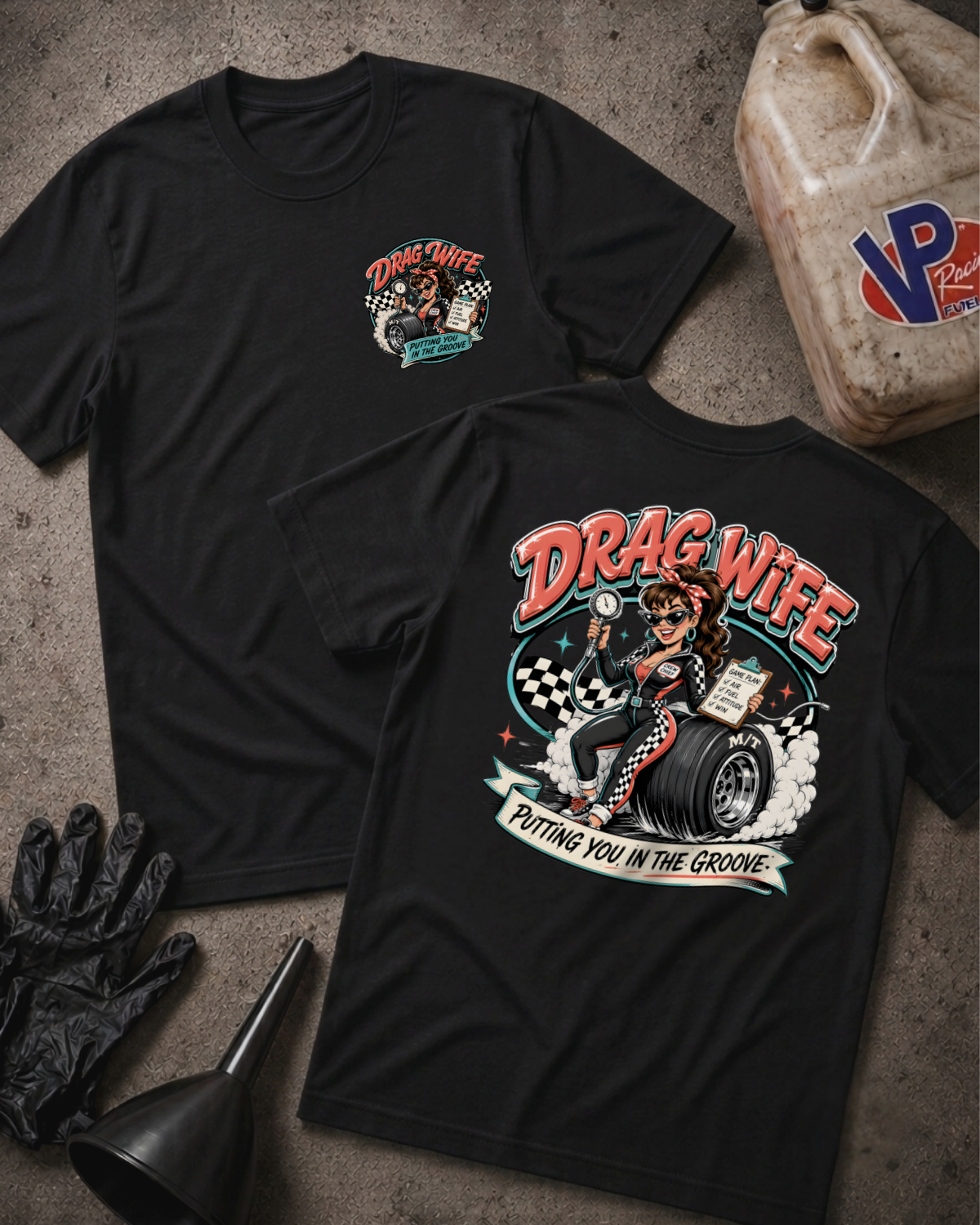 Two black graphic T-shirts laid flat on a textured gray surface, with racing-themed printed artwork and 'Drag Wife Putting You In The Groove' text. A black glove, funnel, and a plastic fuel can are placed around them as styled props.
