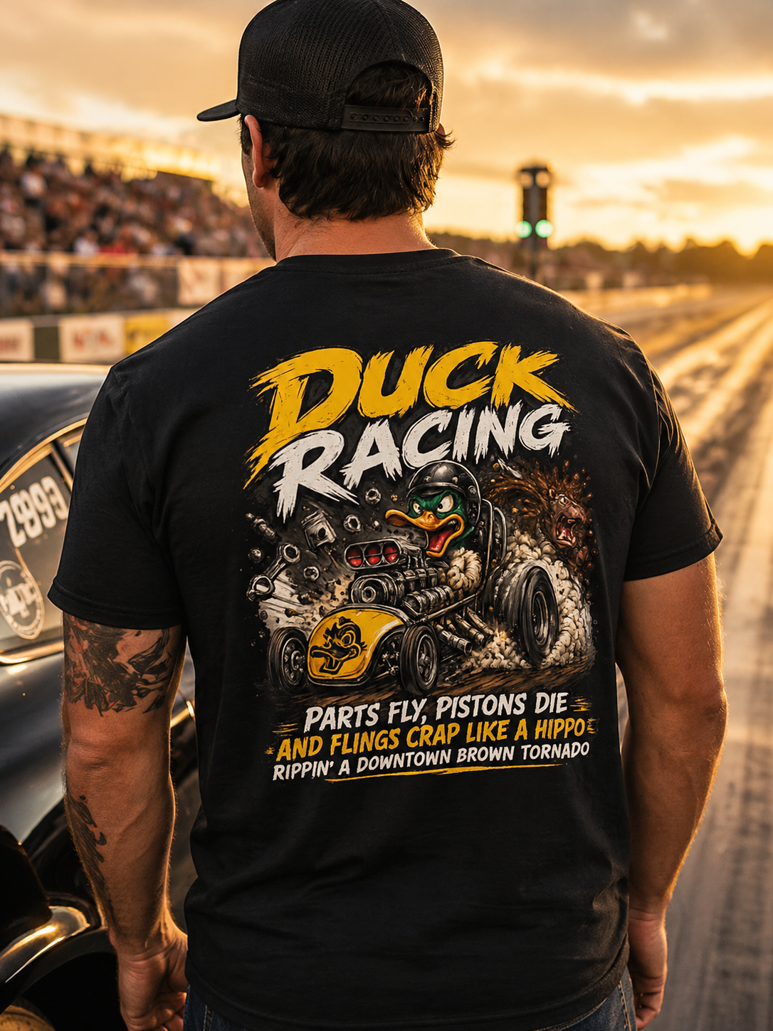 Man wearing a black t-shirt with 'Duck Racing' graphic and text at a race track.
