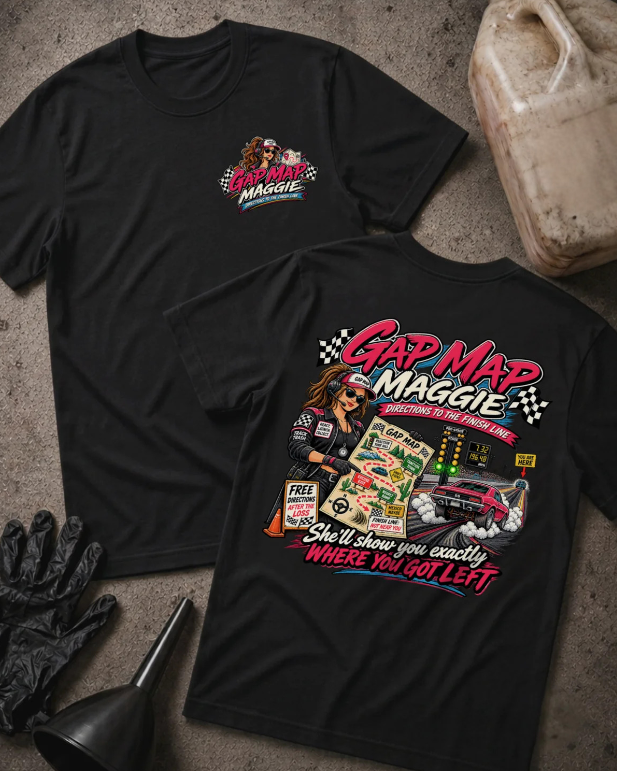 Two black graphic T-shirts laid flat on a concrete surface, showing the front and back designs. The shirts feature a colorful 'Gap Map Maggie' racing graphic with a cartoon woman in a racing suit, checkered flags, a race car, and the phrase 'She'll show you exactly WHERE YOU GOT LEFT'.