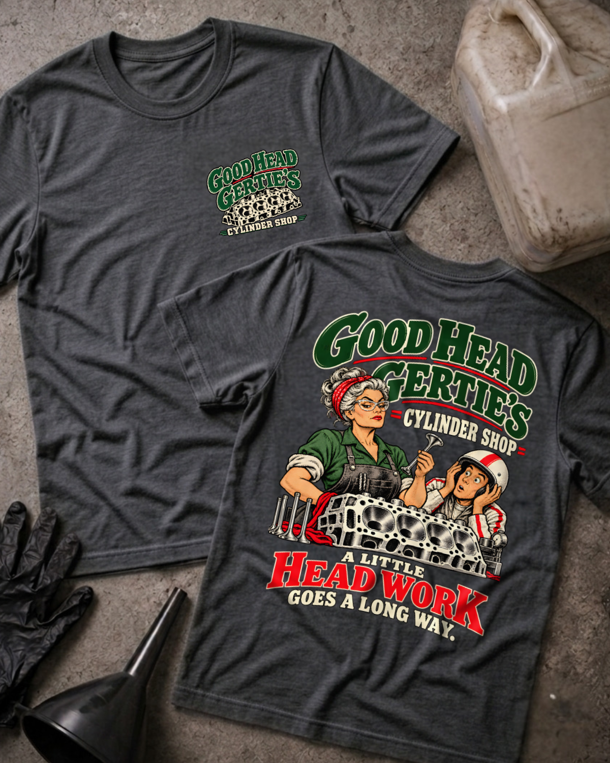 Dark grey heather Good Head Gertie’s Cylinder Shop T-shirt showing the front chest logo and back cartoon of a woman machinist machining a cylinder head beside a racer in a helmet, “A Little Head Work Goes a Long Way,” with gloves, funnel, and oil jug.