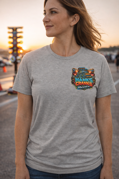 Woman wearing athletic heather Hanks Cranks motorsports t-shirt with small front logo at a drag racing track during golden hour.