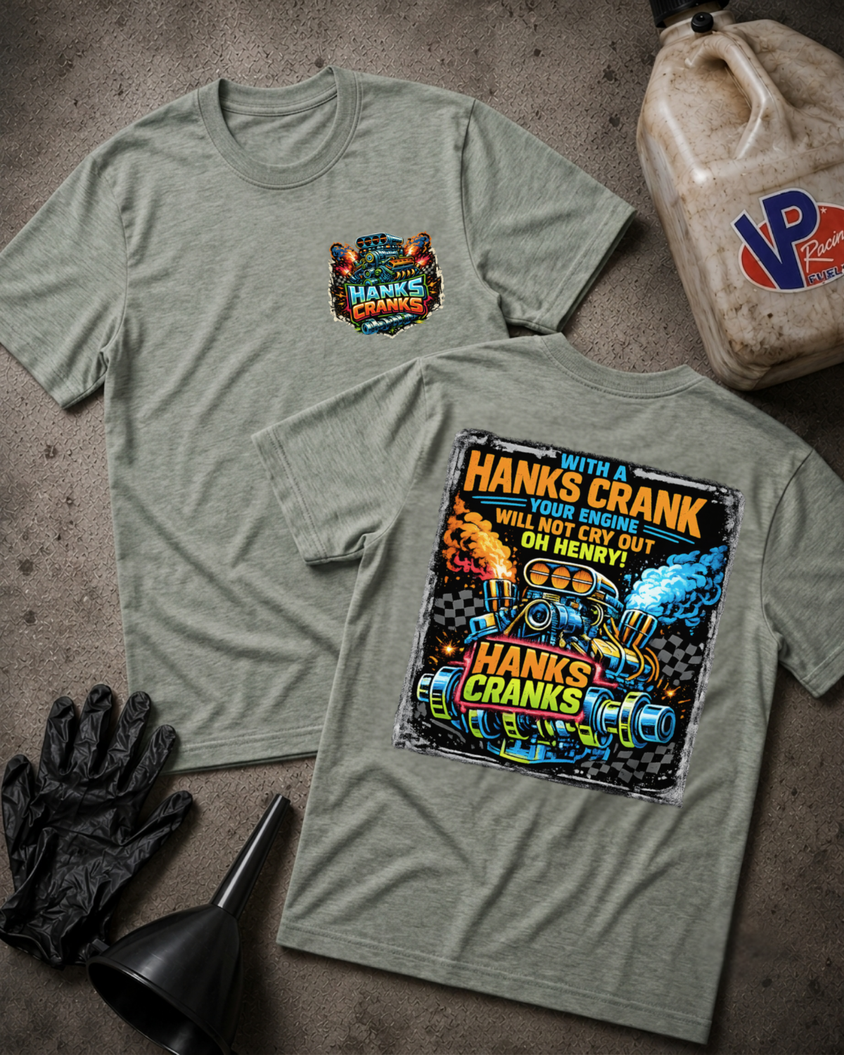 Two athletic heather graphic t-shirts displayed flat on a textured gray surface, surrounded by black gloves, a black funnel, and a plastic jug. The front shirt features a small multicolor chest graphic, while the back shirt features a large, colorful graphic print with the text 'HANKS CRANK'.
