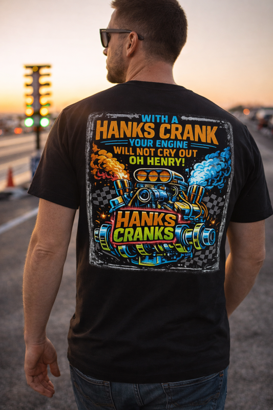 Man standing trackside at a drag strip during golden hour wearing a black Hanks Cranks drag racing t-shirt with large supercharged engine graphic on the back.